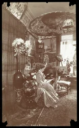 Amelia Bingham seated in her apartment reading, c.1905